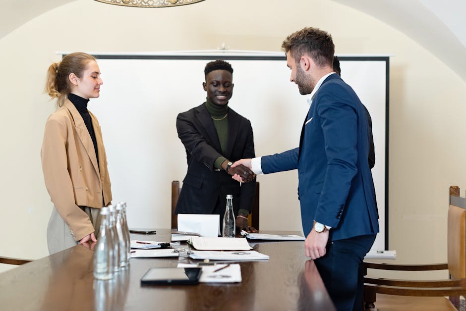 A diverse group of business professionals in a meeting room, shaking hands as a sign of agreement.